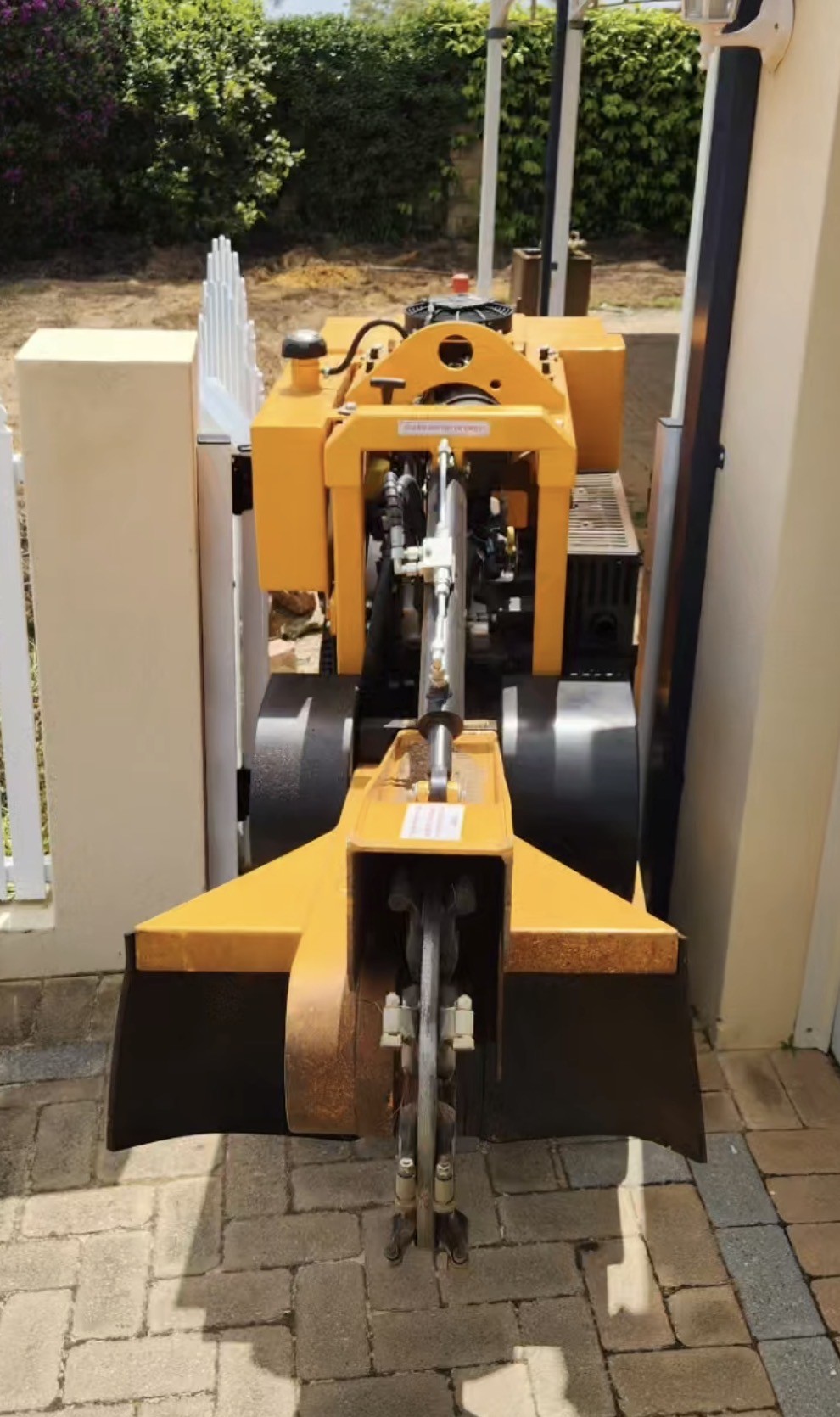 Savvy's yellow tracked stump grinder with its tracks retracted, fitting through a narrow residential side gate