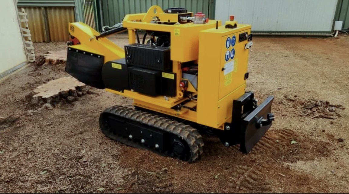 Side view of the compact tracked stump grinder beside a freshly ground stump